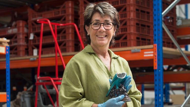 Sara King wears a green shirt and faces the camera, holding the fragment of a blue ceramic statue